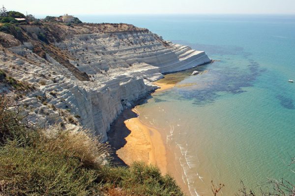 Steep white cliffs meet a sandy beach along a clear turquoise sea.
