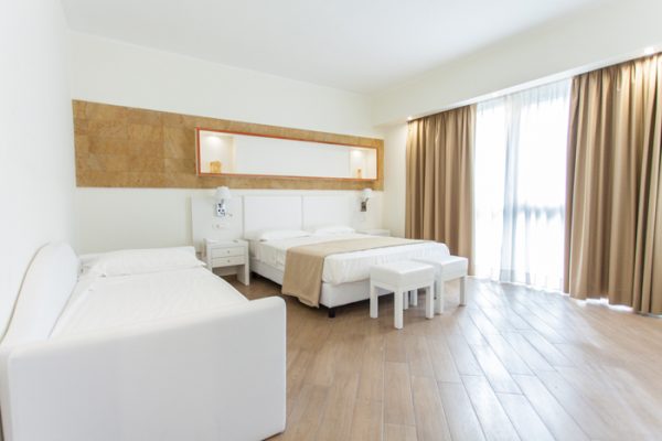 Camera d'albergo spaziosa e luminosa con tre letti e arredamento moderno.